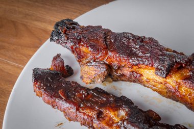 Beyaz bir porselen tabakta barbekü soslu kızarmış domuz kaburgası, grafit ve bıçakla. Tahta masa. Görünümü Kapat.