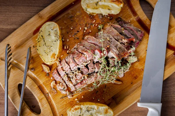FLANK STEAK beef BBQ food. Roasted meat with potatoes and thyme on a wooden board, completely cut into slices. Top view.