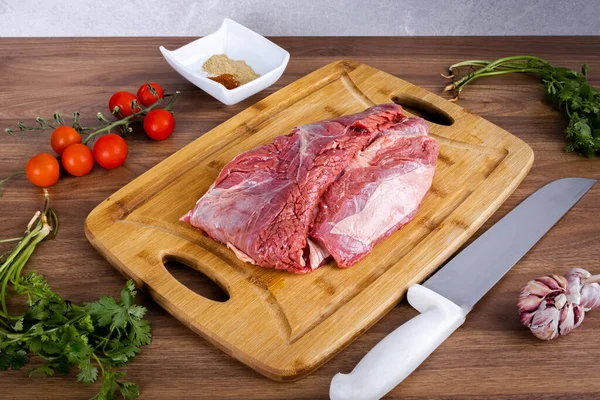 FLANK STEAK beef BBQ food. Raw meat covered with fat on a wooden board on a wooden background. Seasoned with cilantro, garlic and tomatoes. Perspective view.