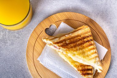 Grilled ham and cheese. Sandwich with cheese and ham on the grill. Served on a wooden board. Accompanied by orange juice.