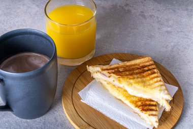 Grilled ham and cheese. Sandwich with cheese and ham on the grill. Served on a wooden board. Accompanied by coffee with milk and orange juice.