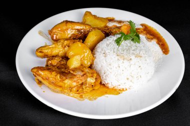 homemade chicken stew with tomato, onion and potato on black fabric table and plate with rice. Perspective view.