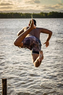 Çocuk nehre atlıyor, arkasında günbatımı var..