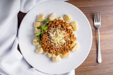 GNOCCHI, domates sosuyla pişirilmiş, rendelenmiş peynirle kaplanmış, ahşap bir tabakta öğütülmüş. Tabağın etrafına beyaz havlu dola..