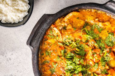 Lezzetli Brezilya balıklı moqueca domates, soğan, zeytinyağı, kişniş ve orocum tohumu. Beyaz masa ve siyah arka planda kilden yapılmış. Pirinçli. Üst görünüm.