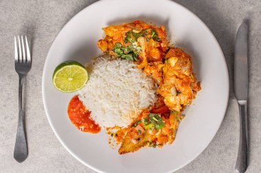 Lezzetli Brezilya balıklı moqueca domates, soğan, zeytinyağı, kişniş ve orocum tohumu. Beyaz bir porselen tabakta pilavla servis edilmiş. Üst görünüm.