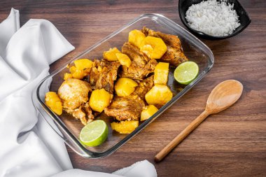 Ahşap bir masada düdüklü tencerede pişmiş domuz pirzolası. Kasenin etrafına beyaz havlu. Pirinç ve tahta kaşık. Perspektif görünümü.