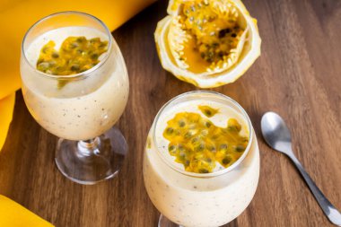 Cam bir kasede tutku meyveli mus, arka planda çarkıfelek meyvesi, ahşap bir masa örtüsü ve sarı bir masa örtüsü. Gümüş kaşık..