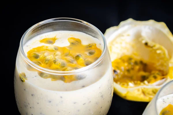 Passion fruit mousse in a glass bowl, with passion fruit in the background, on a black background. Close view.