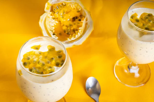 Passion fruit mousse in a glass bowl, with passion fruit in the background, on a Yellow background. Perspective view.