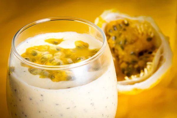 Passion fruit mousse in a glass bowl, with passion fruit in the background, on a yellow background. Close view.