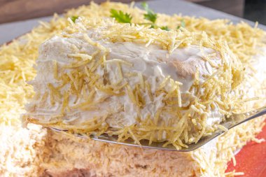 Tipik bir Brezilya yemeği olan dondurulmuş baharatlı tavuk turtası kesiyorum. Kırmızı şekilli, gri ahşap arka planda ve turtanın üzerinde kişniş var..