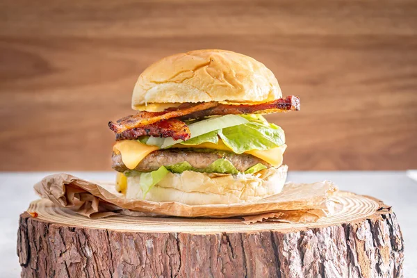 stock image Delicious hamburger with cheddar cheese and bacon over wooden log and wooden background.