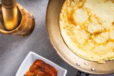 Beyaz bir masada tavada leziz krepler, buğday, yumurta, zeytin yağı, domates sosu ve arka planda kareli masa örtüsü. Üst görünüm.