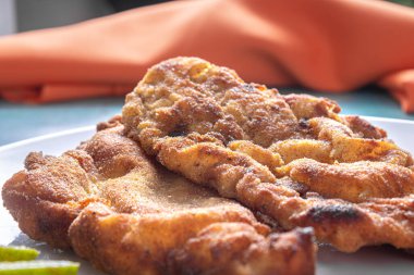 Lezzetli Milano tavuğu (ekmek kırıntıları ve yumurta ile ekilmiş tavuk), tipik bir Brezilya yemeği. Beyaz bir tabakta domatesli, limonlu mavi mermer. Yakın görünüm.