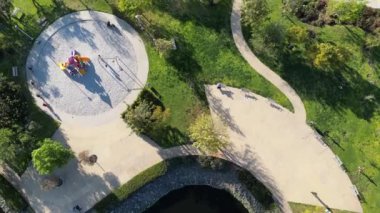 aerial view of a park with lake, fountain, playground with people on bicycles in a late afternoon day, Dron view