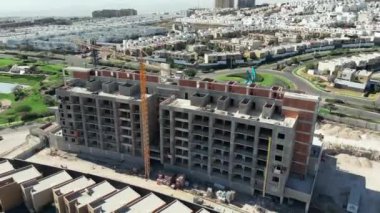 Arkaplanda yeşil bahçeler ve çalışma makineleri olan inşaat halindeki bir binanın havadan görünüşü, dron görünümü