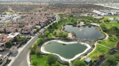 Öğleden sonra gölleri ve yeşil alanları olan bir şehir parkında İHA turu, etrafında evler, dron manzaralı