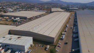 Endüstriyel binaların, depoların hava manzarası. Etrafta kamyonlar, hareket halindeki araçlar, gün batımı, yazın insansız hava aracı manzarası.