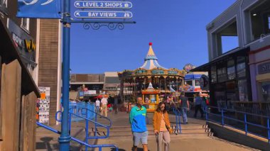 San Francisco, Kaliforniya 'daki 39. İskele' de altın renkli bir atlıkarınca. Çocuklar ve turistler güneşli bir yaz sabahında canlı bir şehir ortamında açık mavi gökyüzüyle ikonik bir cazibenin tadını çıkarıyorlar..