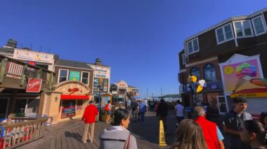 San Francisco, California 'daki 39. rıhtımda turistler ve rıhtım boyundaki renkli dükkanlarla yürüyüş turu. Güneşli bir yaz sabahında açık mavi gökyüzü ile canlı bir turistik mekan gösterirken.
