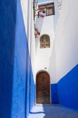 Güneş ışığı, Şef, Fas 'ta dar bir sokağı aydınlatıyor. Canlı mavi duvarlar, ahşap bir kapı ve renkli begonviller sergiliyor.