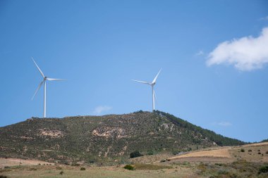 İki rüzgar türbini bir tepenin üstünde sürdürülebilir güç üretimini sembolize ederek yenilenebilir enerji üretiyor.