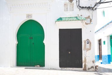 İki zıt kapı, biri canlı yeşil, diğeri koyu siyah, Asilah, Fas 'ta beyazlatılmış bir binada yan yana durarak şehrin eşsiz mimari tarzını gözler önüne seriyor.