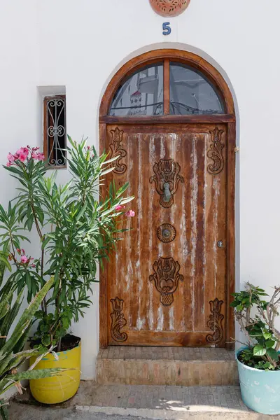 Süslü ahşap kapılar dekoratif oymalar, bitkiler, ve beyaz bir duvarda beş numara, geleneksel mimari detaylar sergileniyor.