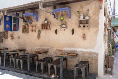 Metal masalar ve tabureler dekore edilmiş duvarları, bitkileri ve asılı ışıkları olan bir restoranın önünde duruyor.