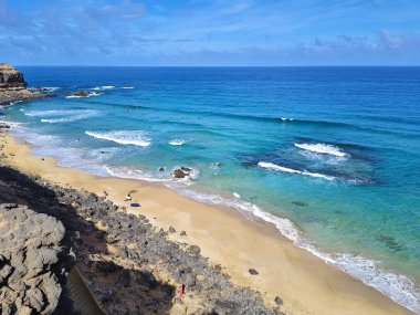 Turkuaz okyanus dalgaları sahilin kumlu sahillerine çarpıyor. Sörfçüler, fuerteventura 'da güneşli havanın tadını çıkarıyor.