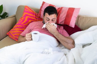 Soğuk algınlığı olan ve koronavirüs hastası olan bir adam çay içiyor.