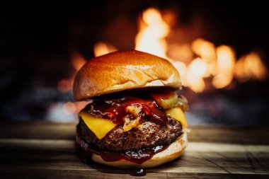 Cheeseburger on a wooden table in front of a fireplace.