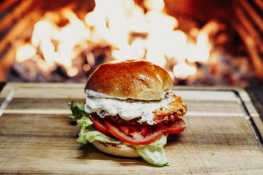 Chicken burger on a wooden table in front of a fireplace.