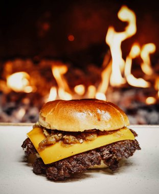 Smashed Cheeseburger on a wooden table in front of a fireplace.