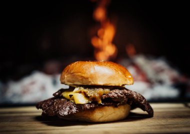 Smashed Cheeseburger on a wooden table in front of a fireplace.