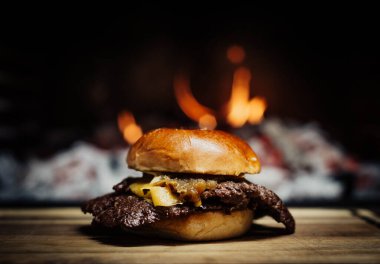 Smashed Cheeseburger on a wooden table in front of a fireplace.