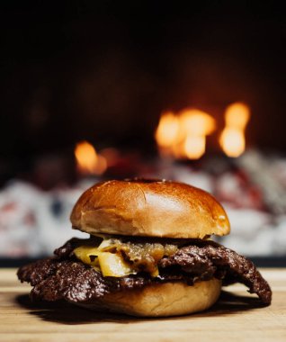 Smashed Cheeseburger on a wooden table in front of a fireplace.
