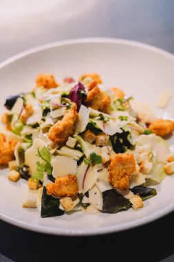 Beyaz tabakta kızarmış ekmek ve peynirli Sezar salatası.