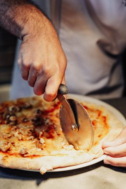 Stajyer şef pizza kesicisi ile harika bir iş çıkarıyor. Herkesin tadını çıkarması için lezzetli dilimler yapıyor.
