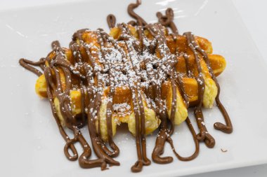 Beyaz tabakta çikolata soslu Belçika waffleları.