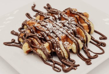 Beyaz tabakta çikolata soslu Belçika waffleları.
