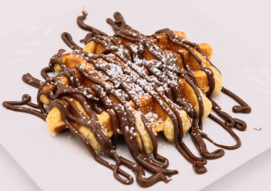 Beyaz tabakta çikolata soslu Belçika waffleları.