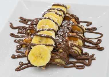 Muz ve çikolatalı waffle bir restoranda beyaz bir tabakta.