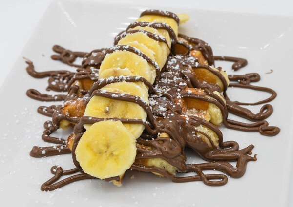 Вафли с бананом и шоколадом на белой тарелке в ресторане