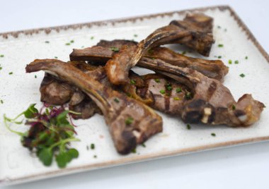 Izgara kuzu pirzolası, taze otlar ve baharatlar beyaz tabakta.