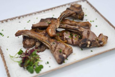 Izgara kuzu pirzolası, taze otlar ve baharatlar beyaz tabakta.