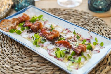 Ahtapot Carpaccio, domates garnitürlü ve beyaz tabakta mikroyeşillik.