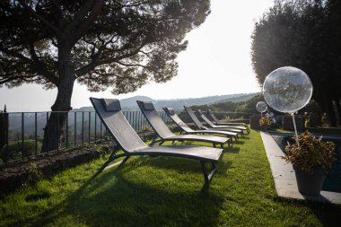 Lüks çiftlik evindeki yüzme havuzunun yanında sıralanmış güneşli yataklar.