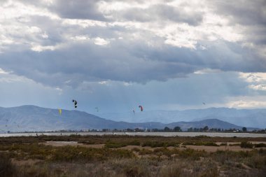Denizde yağmurdan önce dramatik bulutları olan bir sürü uçurtma avcısı, Delta del Ebro 'daki Trabucador sahilinde uçurtmacılar.